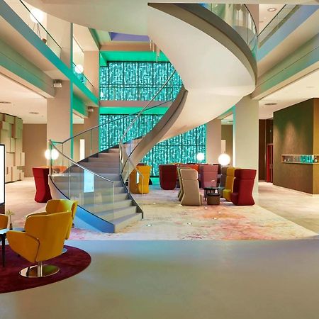 Steigenberger Hotel Am Kanzleramt Βερολίνο Εξωτερικό φωτογραφία The photo shows a modern and stylish interior space, likely a hotel lobby. In the center, there's a prominent curved staircase that leads to an upper level. The walls are adorned with a colorful panel of glass or light, adding a vibrant touch to the 
