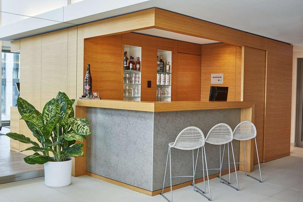 Steigenberger Hotel Am Kanzleramt Βερολίνο Ανέσεις φωτογραφία The photo shows a modern bar area with a sleek design. The bar counter features a combination of wood and stone elements, with a wooden front and a stone-gray top. Behind the counter, there are shelves displaying various bottles, suggesting a selecti