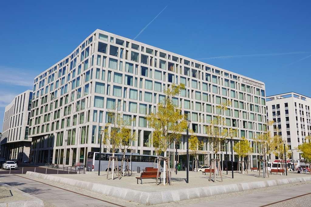 Steigenberger Hotel Am Kanzleramt Βερολίνο Εξωτερικό φωτογραφία The image shows a modern building with a distinctive architectural design. The building has large glass windows arranged in a grid pattern, giving it a sleek and contemporary look. In front of the building, there are several small, leafy trees and be