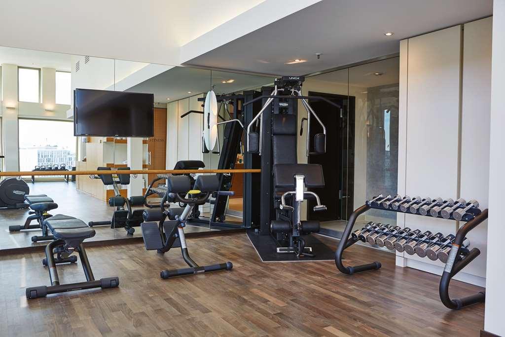 Steigenberger Hotel Am Kanzleramt Βερολίνο Ανέσεις φωτογραφία The photo shows a modern gym or fitness area. It features various exercise equipment, including a multi-gym machine with multiple stations for strength training, a set of dumbbells on a rack, and several workout benches. There is a large mirror refle