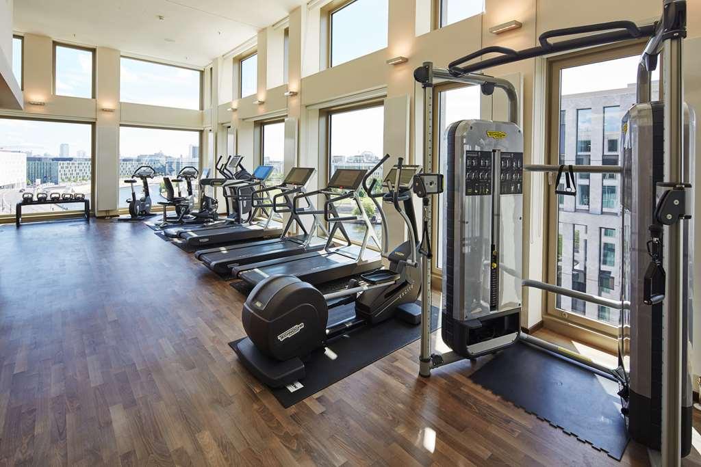 Steigenberger Hotel Am Kanzleramt Βερολίνο Ανέσεις φωτογραφία The photo shows a well-lit gym or fitness area with large windows allowing natural light to flow in. The gym is equipped with various exercise machines, including treadmills and elliptical trainers. There is also a multi-station strength training mac