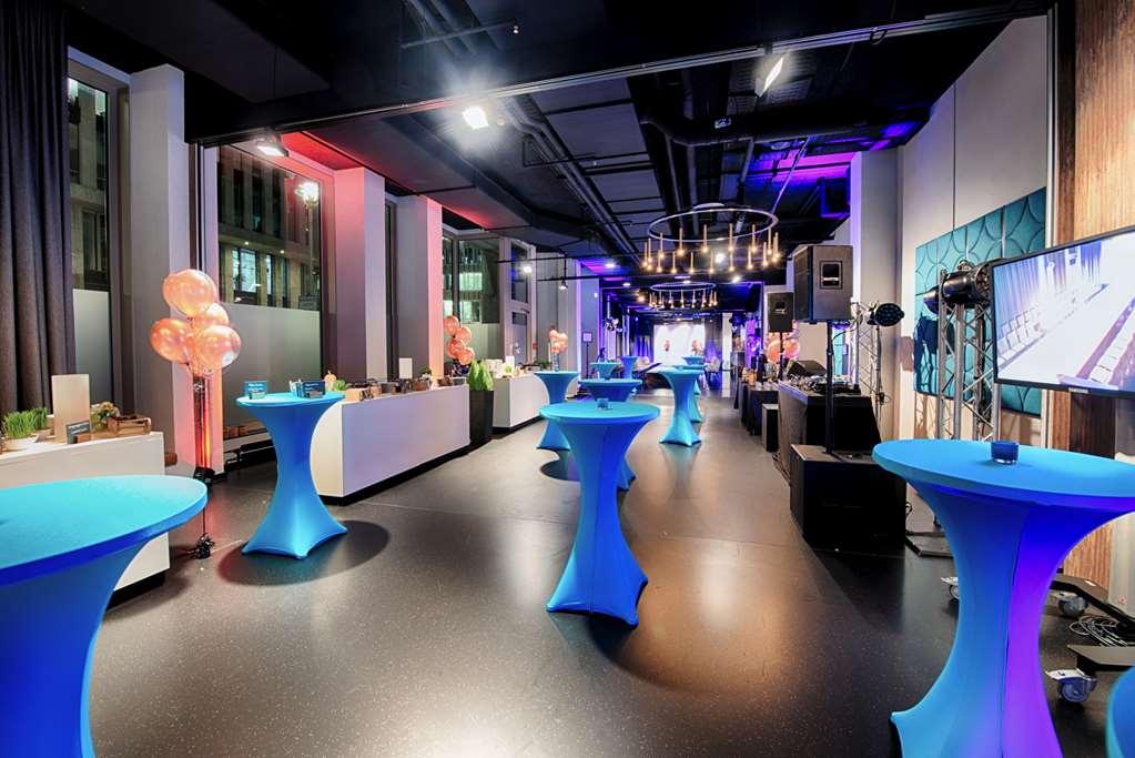 Steigenberger Hotel Am Kanzleramt Βερολίνο Ανέσεις φωτογραφία The photo shows a spacious event venue with modern decor, featuring several tall, round tables covered in blue tablecloths. The area is well-lit with a combination of soft ambient lighting and colorful spotlights, creating a vibrant atmosphere. There