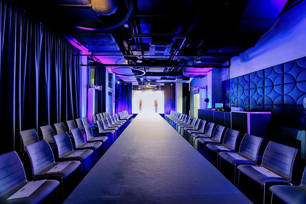 Steigenberger Hotel Am Kanzleramt Βερολίνο Ανέσεις φωτογραφία The photo shows a fashion runway setup. There's a long, narrow runway stretching down the center, flanked by rows of modern chairs on either side. The space is dimly lit, with dramatic purple and blue lighting creating an atmosphere suited for a fash