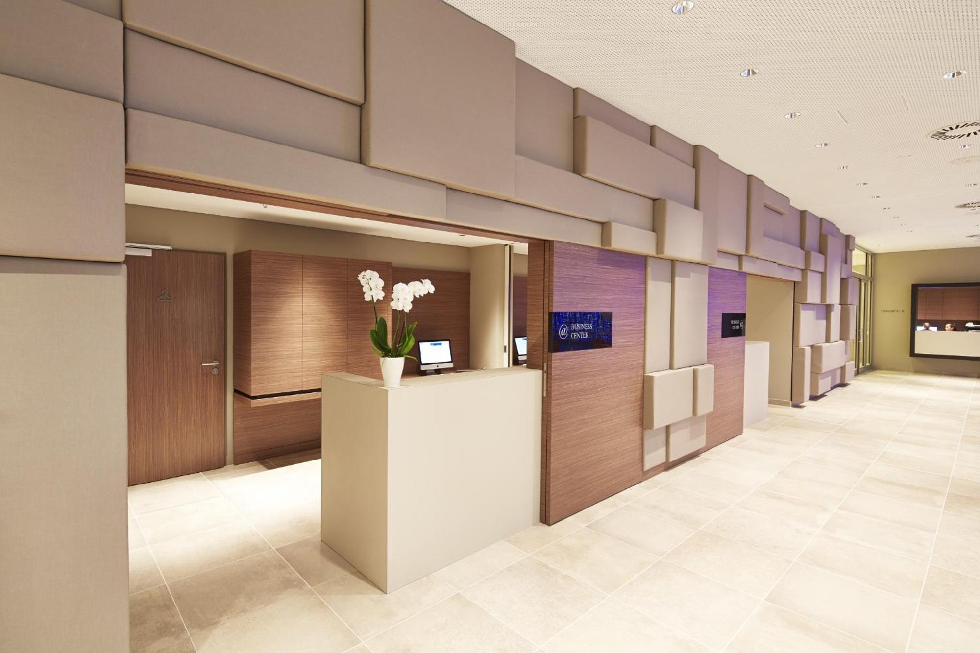 Steigenberger Hotel Am Kanzleramt Βερολίνο Εξωτερικό φωτογραφία The photo shows a modern reception area with a sleek design. The walls are decorated with a mix of beige and brown panels that create a textured appearance. To the left, there is a reception desk with a minimalist style, featuring a small plant with 