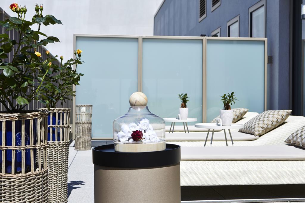 Steigenberger Hotel Am Kanzleramt Βερολίνο Εξωτερικό φωτογραφία The photo showcases a stylish outdoor space, likely a rooftop terrace or balcony. In the foreground, there is a decorative glass dome containing flowers, placed on a sleek circular table. Surrounding this feature are several comfortable lounge chairs
