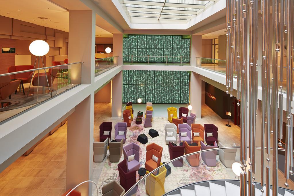 Steigenberger Hotel Am Kanzleramt Βερολίνο Εξωτερικό φωτογραφία The photo depicts a modern interior space, likely a hotel or a lounge area. There are several seating arrangements featuring colorful chairs in various shades, including purple, orange, and yellow. The layout is open and spacious, with natural light 