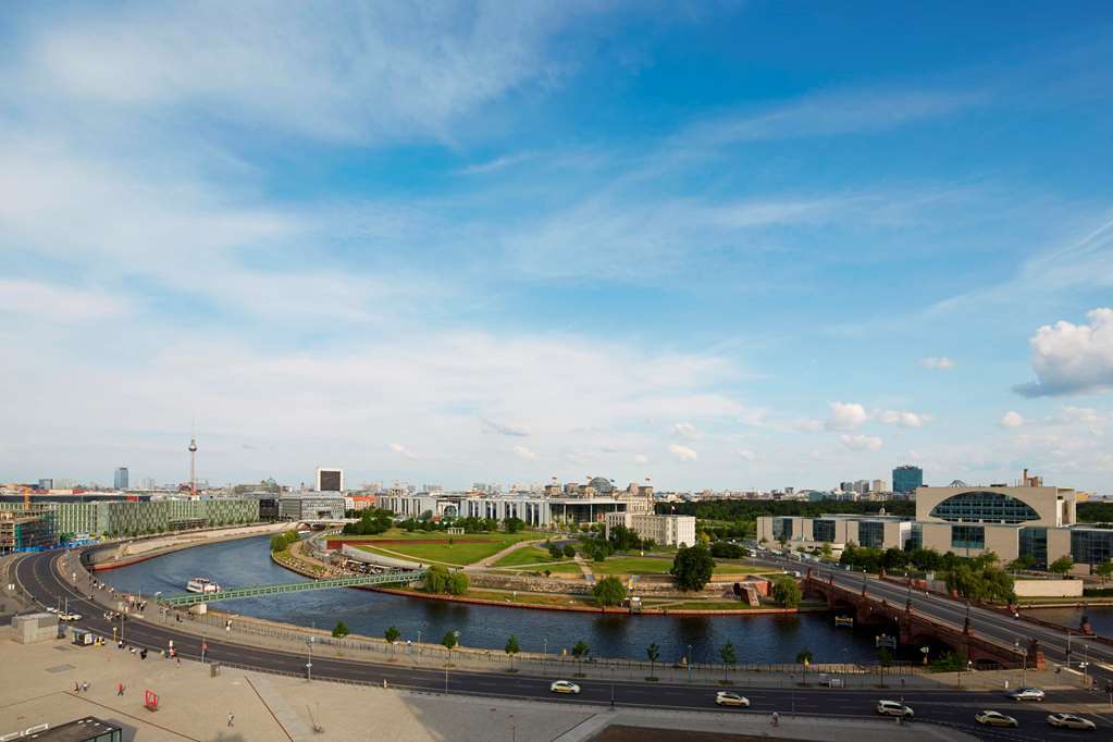 Steigenberger Hotel Am Kanzleramt Βερολίνο Εξωτερικό φωτογραφία The photo depicts a panoramic view of a cityscape featuring a river that winds through the landscape. On one side of the river, there are green spaces with trees and grass, suggesting an area designed for leisure or parks. Along the riverbank, you ca
