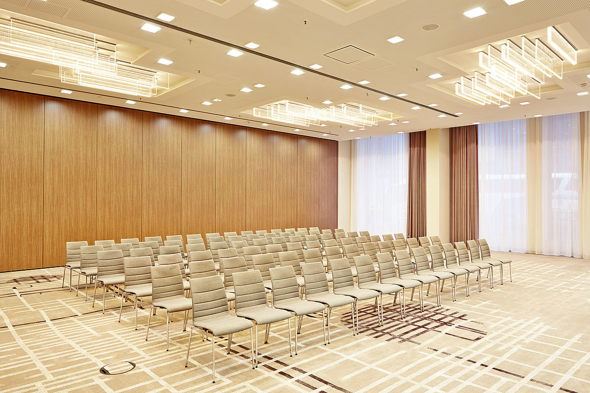 Steigenberger Hotel Am Kanzleramt Βερολίνο Εξωτερικό φωτογραφία The photo shows a conference room set up with rows of light-colored chairs arranged in a neat formation. The walls feature a warm wood finish, contrasting with the soft, neutral tones of the chairs and carpet. There are large windows dressed with lig