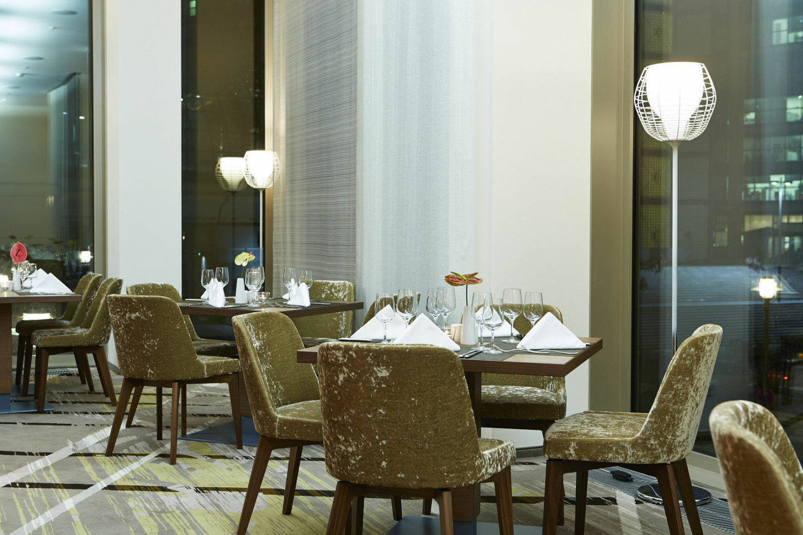 Steigenberger Hotel Am Kanzleramt Βερολίνο Εξωτερικό φωτογραφία The photo shows a stylish dining area in a restaurant. There are several tables set for guests, each adorned with white tablecloths, folded napkins, and glasses. The chairs are upholstered in a muted, plush fabric, giving a cozy yet elegant feel. The