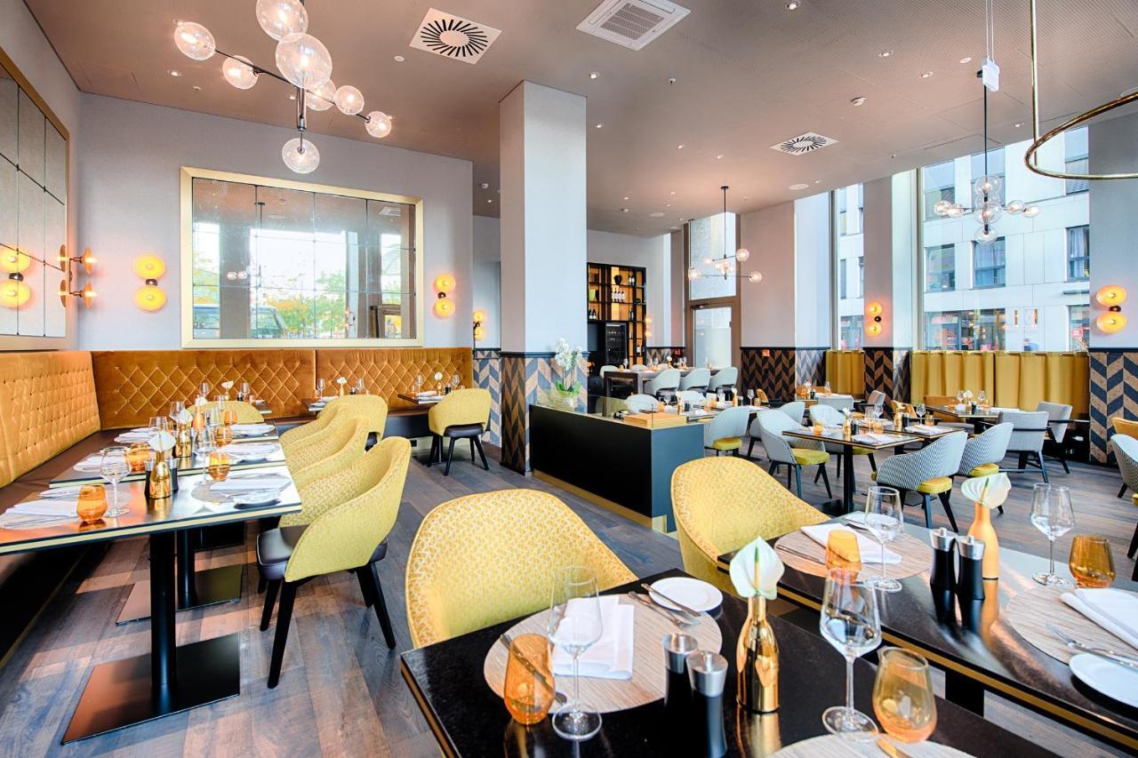 Steigenberger Hotel Am Kanzleramt Βερολίνο Εξωτερικό φωτογραφία The photo showcases a modern restaurant interior. It features a combination of stylish furniture, including round tables with black surfaces and yellow upholstered chairs. The decor includes elegant lighting, with large pendant lights hanging from th
